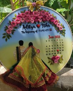 a woman is standing in front of a sign with flowers on it and a calendar behind her