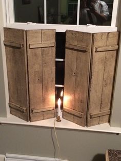 two wooden shutters open to reveal a lit candle in front of a man looking out the window