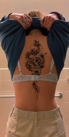 a woman with a dragon tattoo on her back is standing in front of a shower