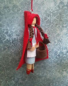 a doll hanging from a wall with a red cape on it's head and a basket in her hand