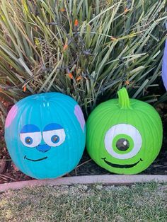 three pumpkins with faces painted on them sitting in front of some plants and bushes