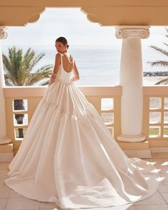 a woman in a wedding dress is standing on a balcony overlooking the ocean and palm trees