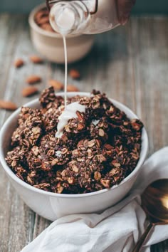 a bowl filled with granola and milk being poured into it