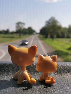 two small toy cats sitting on the dashboard of a car in front of a road