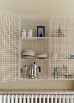 a white radiator sitting next to a shelf filled with dishes and cups on top of it