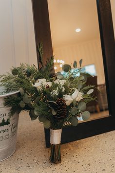 a bouquet of flowers sitting on top of a counter next to a mirror and cup