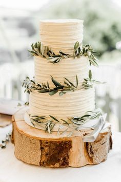 a white wedding cake with greenery on top sits on a wooden slice at the reception table