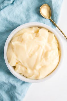 a white bowl filled with cream on top of a blue towel next to a spoon