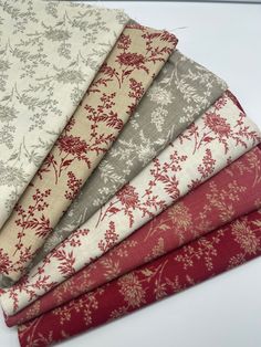 four different fabrics are stacked on top of each other, one is red and the other has white flowers