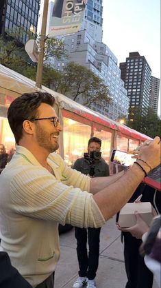 a man holding something in his right hand while standing on the sidewalk with other people