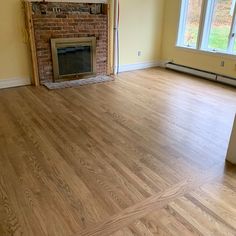 an empty living room with hard wood flooring and a brick fireplace in the corner