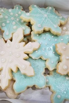 several decorated cookies are in a box on the table, one is frosted and the other has snowflakes