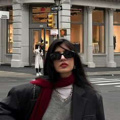 a woman wearing sunglasses and a scarf standing in front of a tall building on a city street