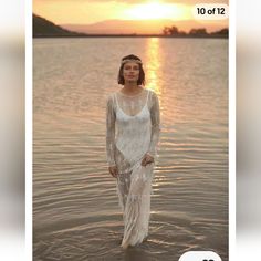 a woman is standing in the water wearing a white dress with sheer sleeves and an embellished headband