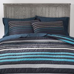 a bed with blue and grey striped comforter set on it's headboard