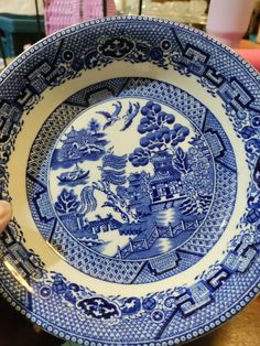 a blue and white plate sitting on top of a table next to a person's hand