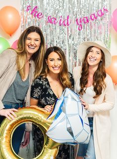 three women posing for the camera with balloons and streamers behind them