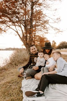 a man and woman are sitting on a blanket with their two children in front of a tree