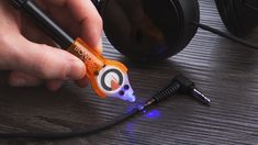 a person holding an orange and white object near headphones on a wooden table with blue light