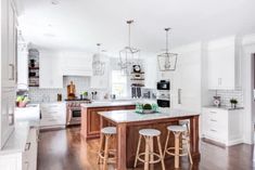 a large kitchen with white cabinets and wooden flooring, an island in the middle is surrounded by bar stools