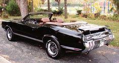 an old black car parked on the side of the road in front of some trees