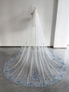 a white wedding veil with blue flowers on the bottom is hanging in an empty room