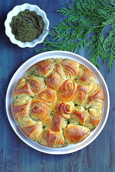 a baked pastry in a white dish next to some herbs and seasoning on a blue table