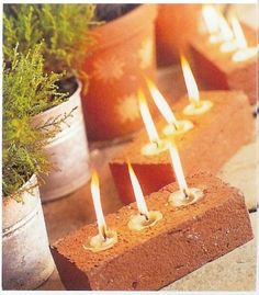 there are many candles that are lit on the bricks in front of potted plants