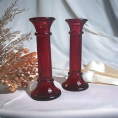 two red glass candlesticks sitting on top of a white table cloth next to a christmas tree