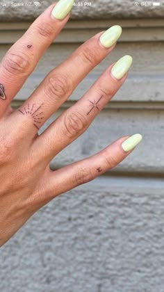 a woman's hand with yellow nails and tattoos on her left thumb, showing the ring finger