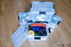 two plastic storage containers filled with yarn and scissors on a hard wood flooring surface