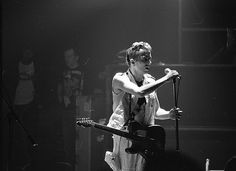 a young man holding a guitar while standing on top of a stage in front of microphones