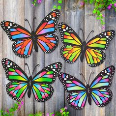 four colorful butterflies sitting on top of a wooden fence next to purple and green flowers