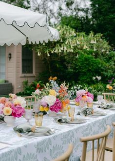 a table set with flowers and plates under an umbrella