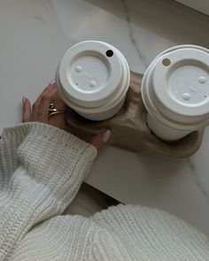 a woman is holding two coffee cups in her hands