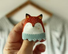 a hand holding a small red and white fox figurine