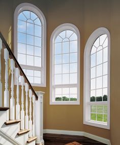 an empty room with three arched windows and hardwood floors, along with a staircase leading up to the second floor