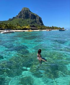 a person swimming in the ocean near a mountain