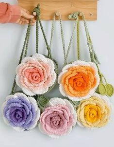 four crocheted flowers hanging from a hook on a white wall next to a person's hand