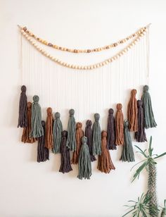 a wall hanging with tassels and beads in various colors on the wall next to a potted plant