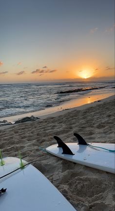 two surfboards sitting on top of a beach next to the ocean at sunset or dawn