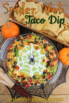 a spider web taco dip with tortilla chips and pumpkins