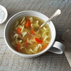 a white bowl filled with pasta and carrots next to a spoon on a wooden table