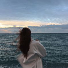 a woman standing on the edge of a boat looking out at the ocean with her hair blowing in the wind