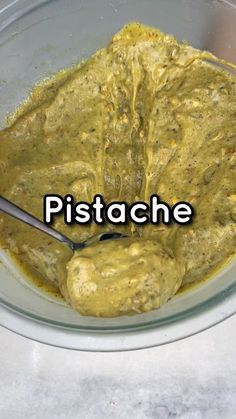 a glass bowl filled with yellow sauce on top of a white counter next to a metal spoon