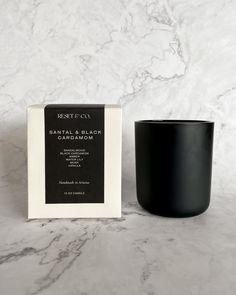 a black candle sitting next to a white box on a marble counter top with the words driftwood and junkner printed on it