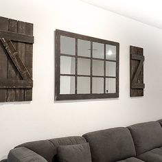 a living room with couches and mirrors hanging on the wall above it's windows