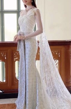 a woman in a white wedding dress standing next to a window with a veil on her head