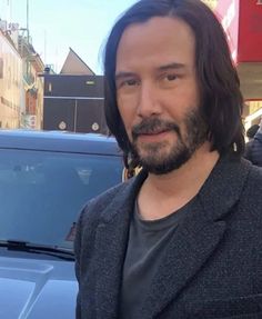 a man with long hair standing in front of a car