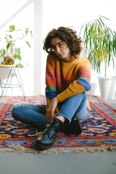 a woman sitting on top of a rug next to a potted plant